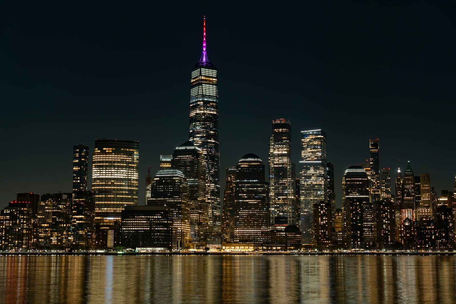 The Manhattan skyline lit up at night, reflected in the water